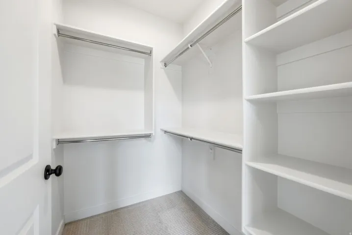 Walk-in closet featuring white built-in shelving, chrome hanging rods, and light-toned carpet flooring