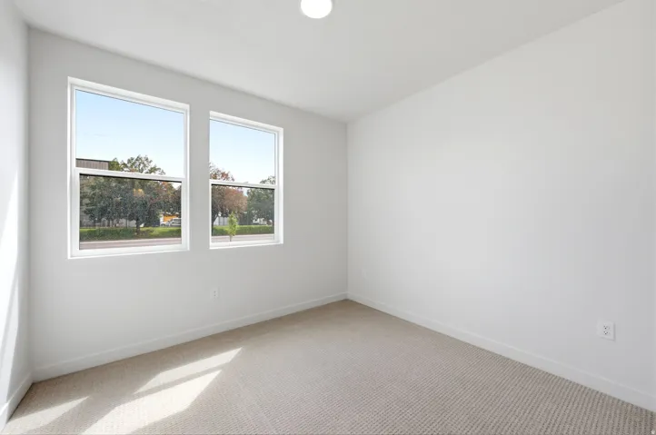 Recessed ceiling light, two large windows, neutral carpeting, and white wall finishes