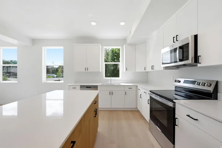 Bright kitchen featuring white cabinetry, stainless steel appliances, a center island with a light wood-finish base, light-toned countertops, and wood-finish flooring