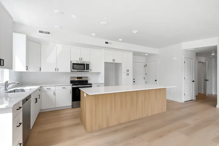 Contemporary kitchen featuring white cabinetry, light countertops, wood-finish flooring, a central island, and stainless steel appliances