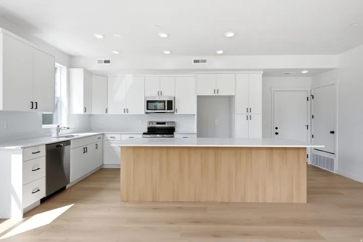 Modern kitchen featuring white cabinetry, light wood-finish flooring, stainless steel appliances, a center island with a light wood finish, and recessed lighting