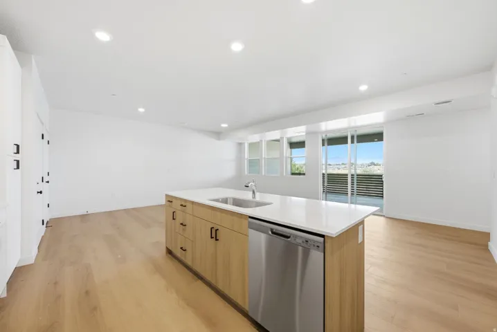 Kitchen island featuring a stainless steel sink, integrated dishwasher, and light wood-finish cabinetry