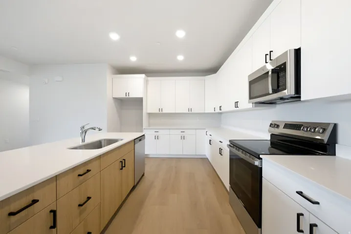 Modern kitchen with wood-finish flooring, white cabinetry, integrated stainless-steel appliances, a kitchen island with a built-in sink, and recessed lighting