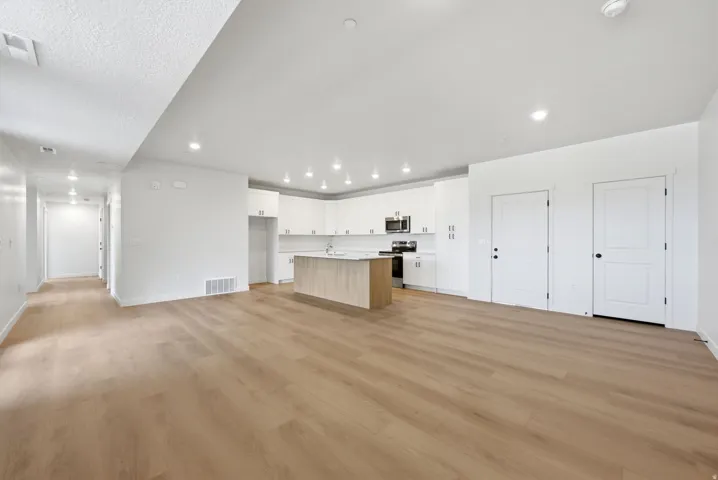 Open-concept living space featuring wood-finish flooring, recessed lighting, a kitchen island with a light-toned base, white cabinetry, and stainless steel appliances