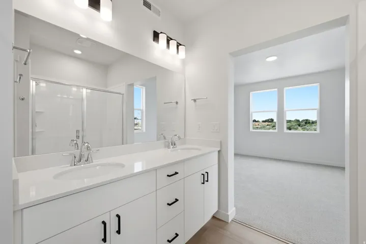 Double vanity with white cabinetry, polished chrome fixtures, and a large wall-mounted mirror