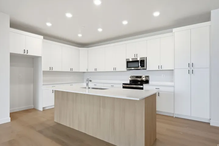 Kitchen featuring white cabinetry, stainless steel appliances, a center island with sink, light-toned wood-finish flooring, and recessed lighting