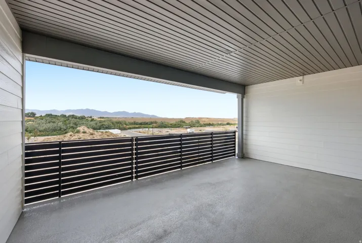 Modern covered patio with polished concrete flooring, black horizontal metal railings, corrugated metal ceiling, and expansive vistas of open countryside and distant mountains