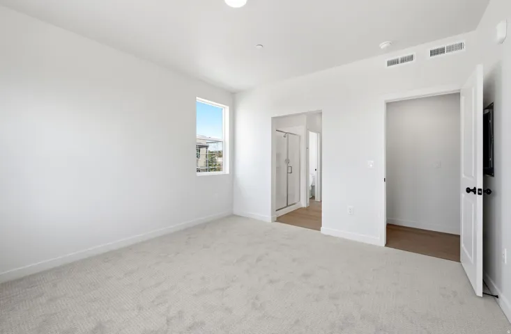 Plush carpeting, window with outdoor scenery, recessed ceiling lighting, access to a full bathroom with a glass-enclosed shower, and a separate closet with wood-finish flooring