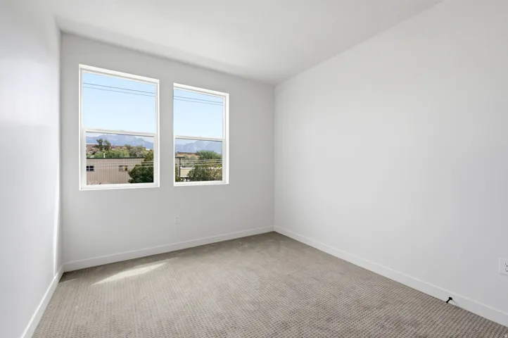 Two large windows, light gray wall-to-wall carpeting, and white painted walls