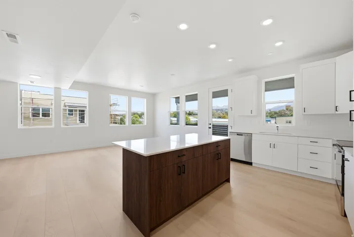 White cabinetry with matte black hardware, stainless steel appliances, a large center island with a light-toned countertop, wood-finish flooring, and multiple windows
