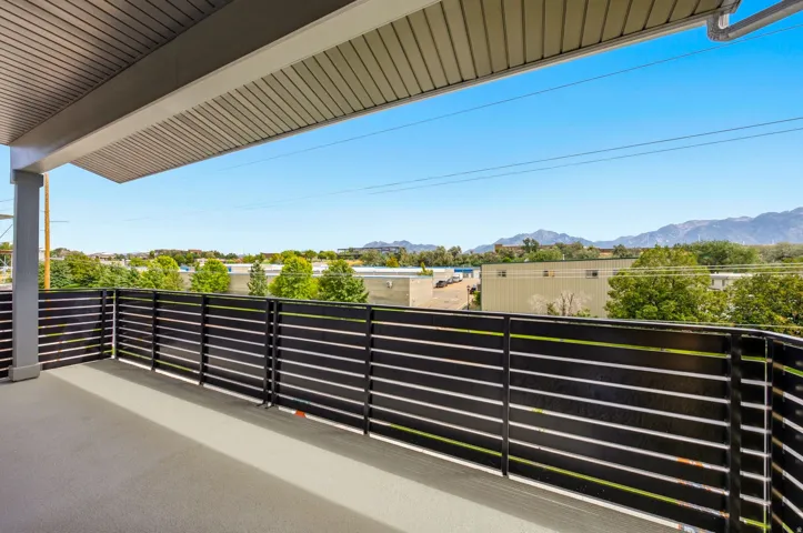 Expansive balcony featuring contemporary slatted railing, covered overhead structure, and distant mountain scenery