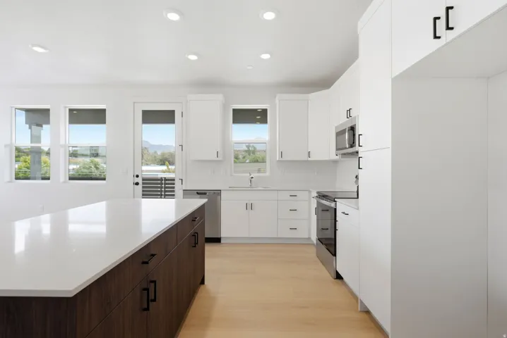 Kitchen featuring a large island with white countertop, white cabinetry, integrated stainless steel appliances, and wood-finish flooring