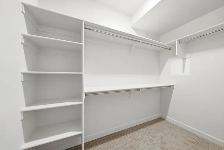 Built-in shelving, multiple hanging rods, and neutral carpet flooring