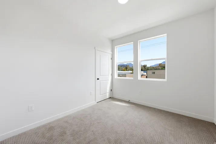 Recessed ceiling light, two double-hung windows, white paneled door with black hardware, light-toned carpeting, and a mountain backdrop