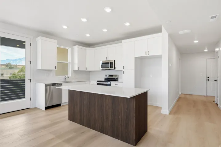Kitchen featuring white cabinetry, light wood-finish flooring, a central island with a white countertop, stainless steel appliances, and recessed lighting