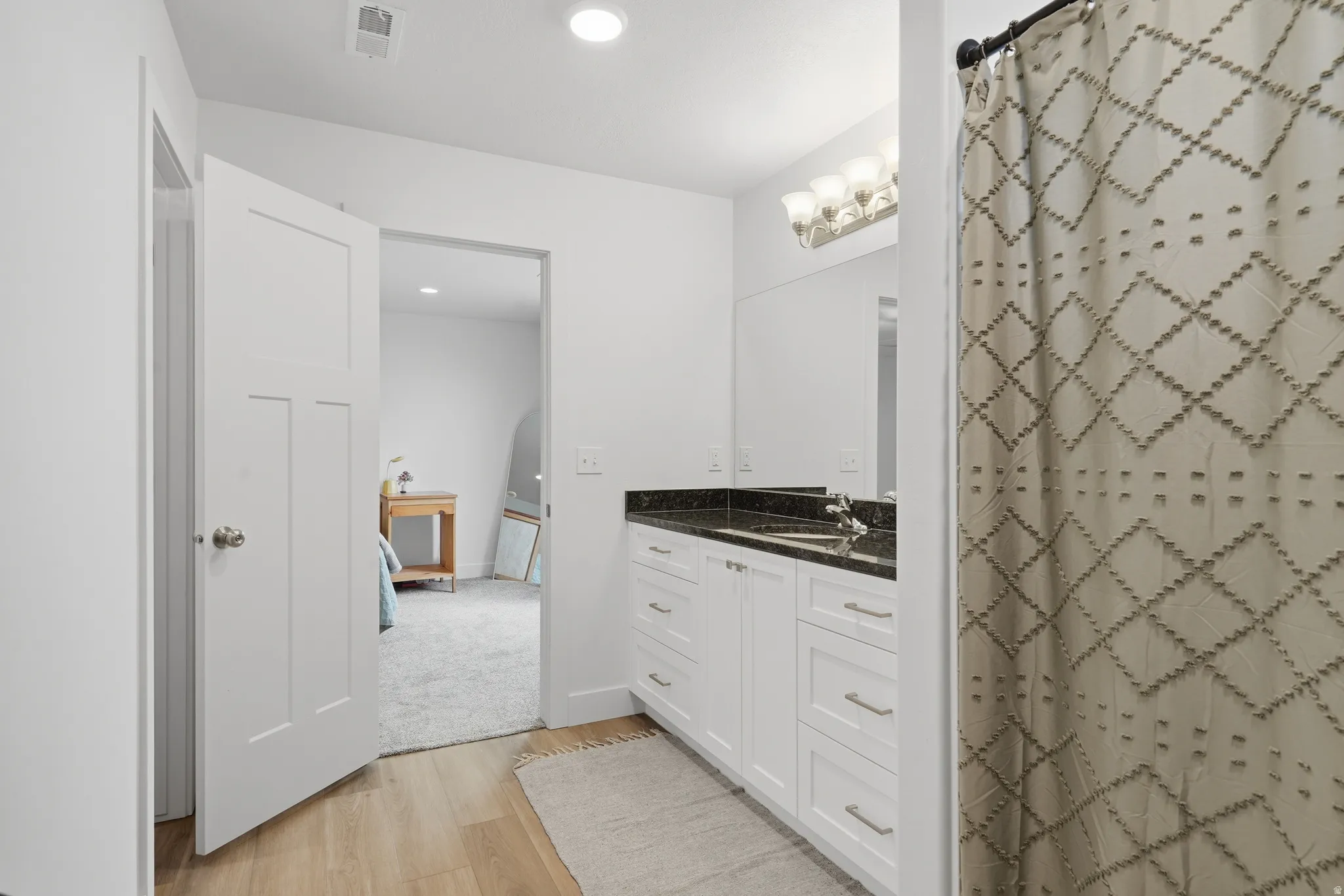 Wood-finish flooring, white paneled doors, recessed lighting, double vanity with dark countertop, and brushed nickel hardware