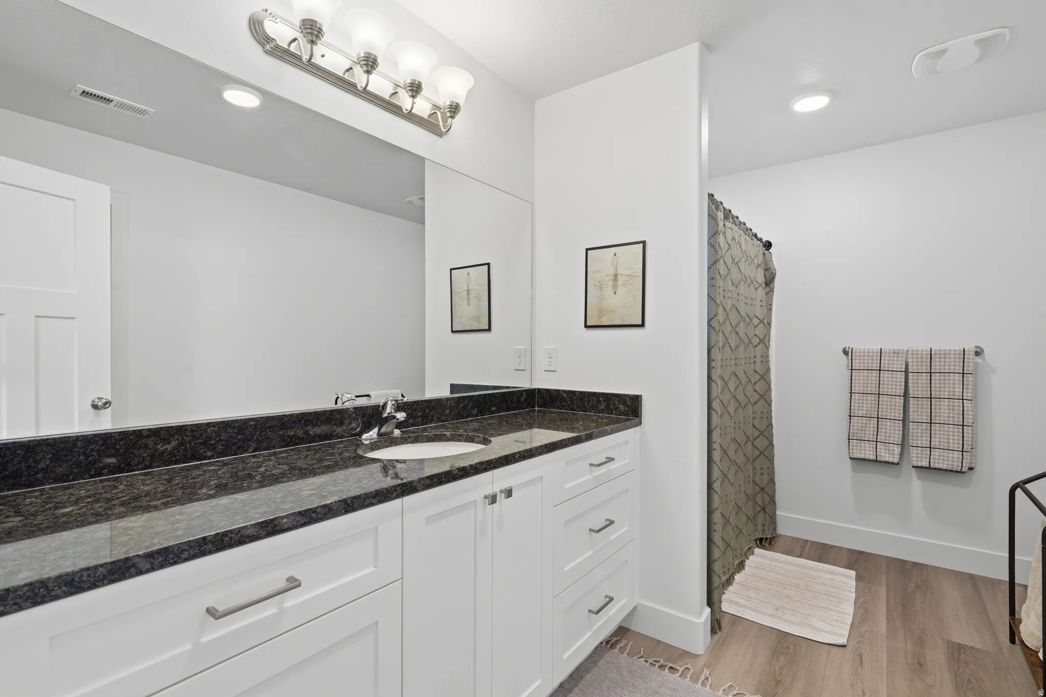 Spa-inspired primary bathroom featuring a double-sink vanity with white cabinetry, black stone countertops, and polished nickel hardware