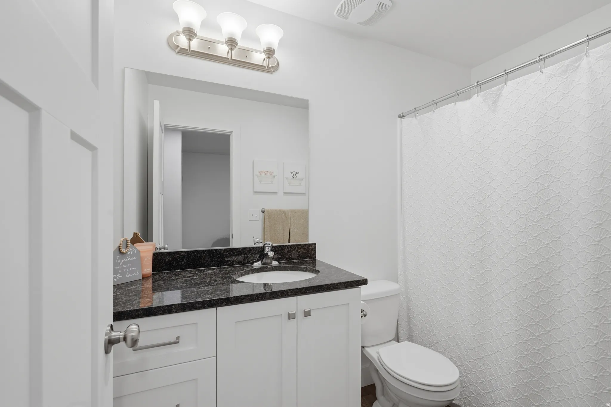 White shaker-style vanity with dark countertop, undermount sink, and brushed nickel hardware