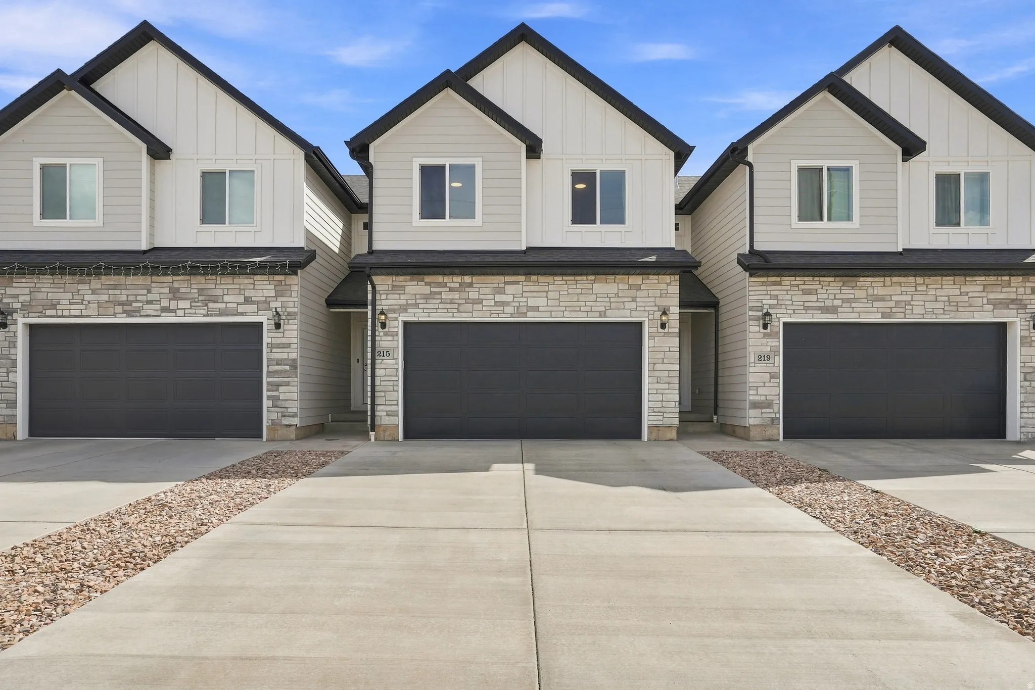 Modern exterior with board and batten siding, stone veneer accents, dark trim, and dark garage doors