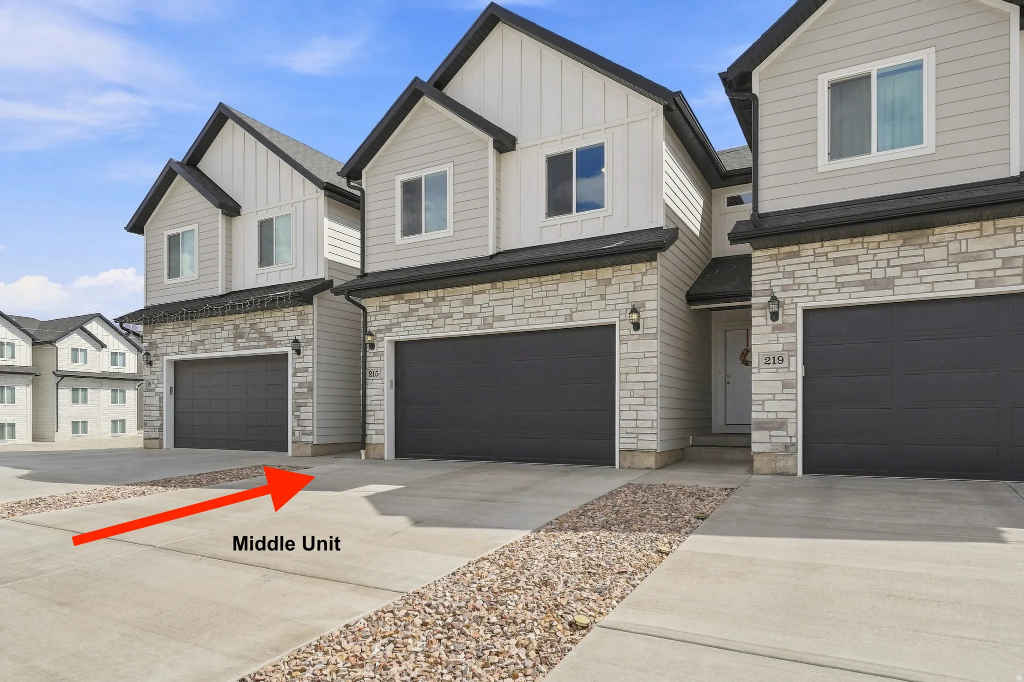 Two-story exterior with light gray siding, stone veneer accents, dark gray garage door, and concrete driveway