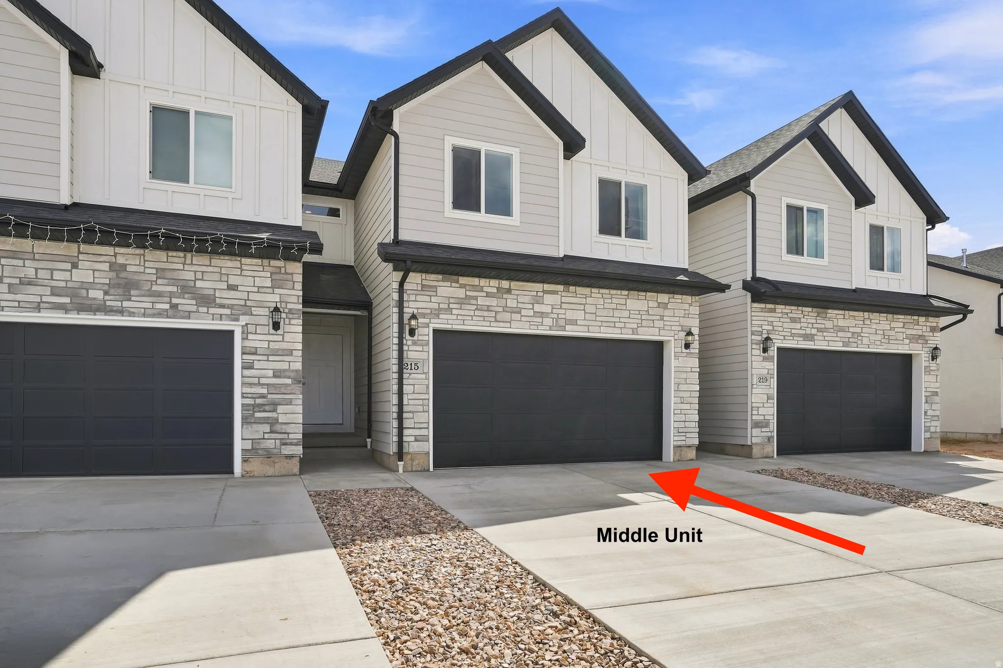 Contemporary townhome exterior featuring stone accents, vertical and horizontal siding, a dark garage door, and concrete driveway