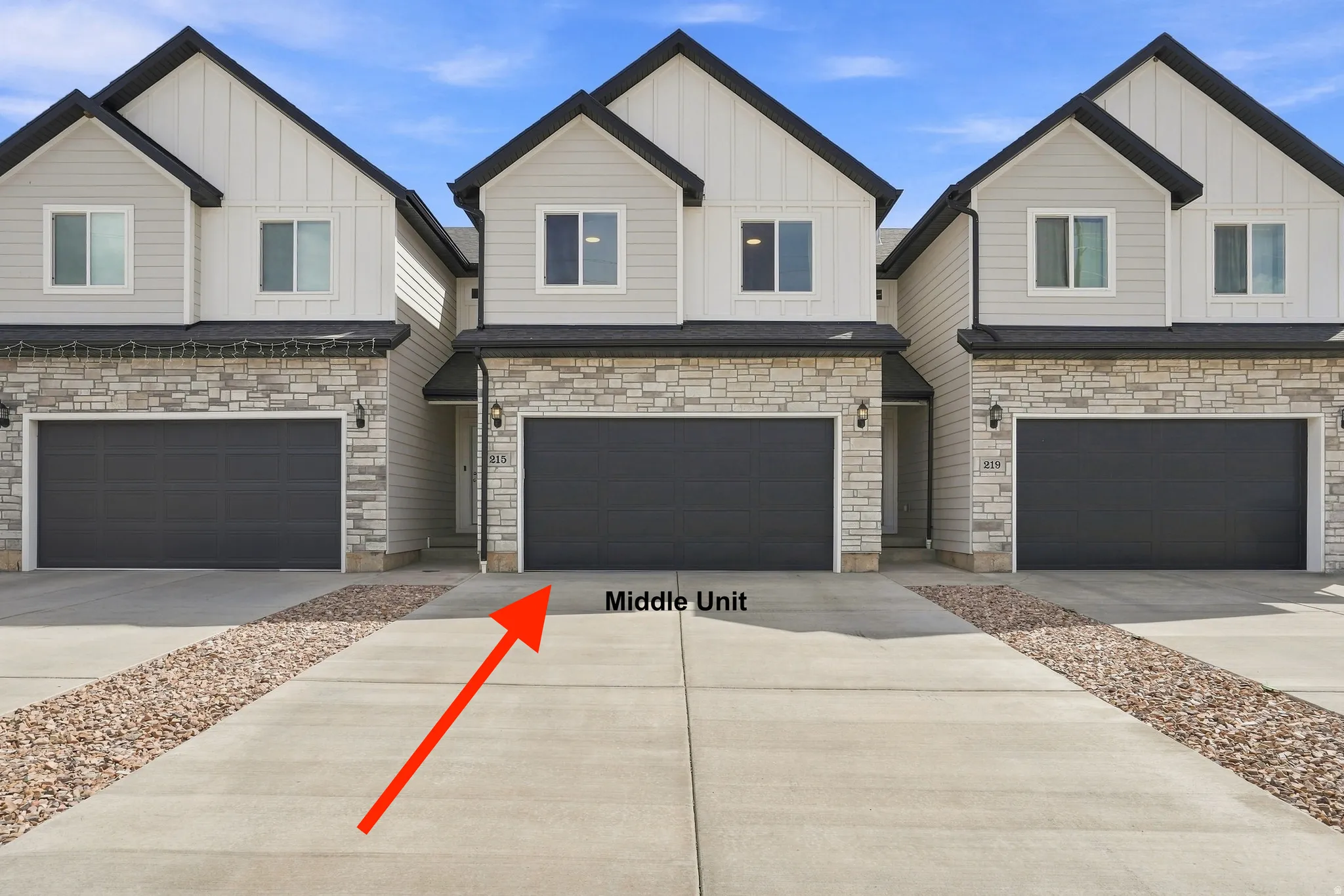 Contemporary exterior with light gray siding, stone accents, black trim, and a two-car garage