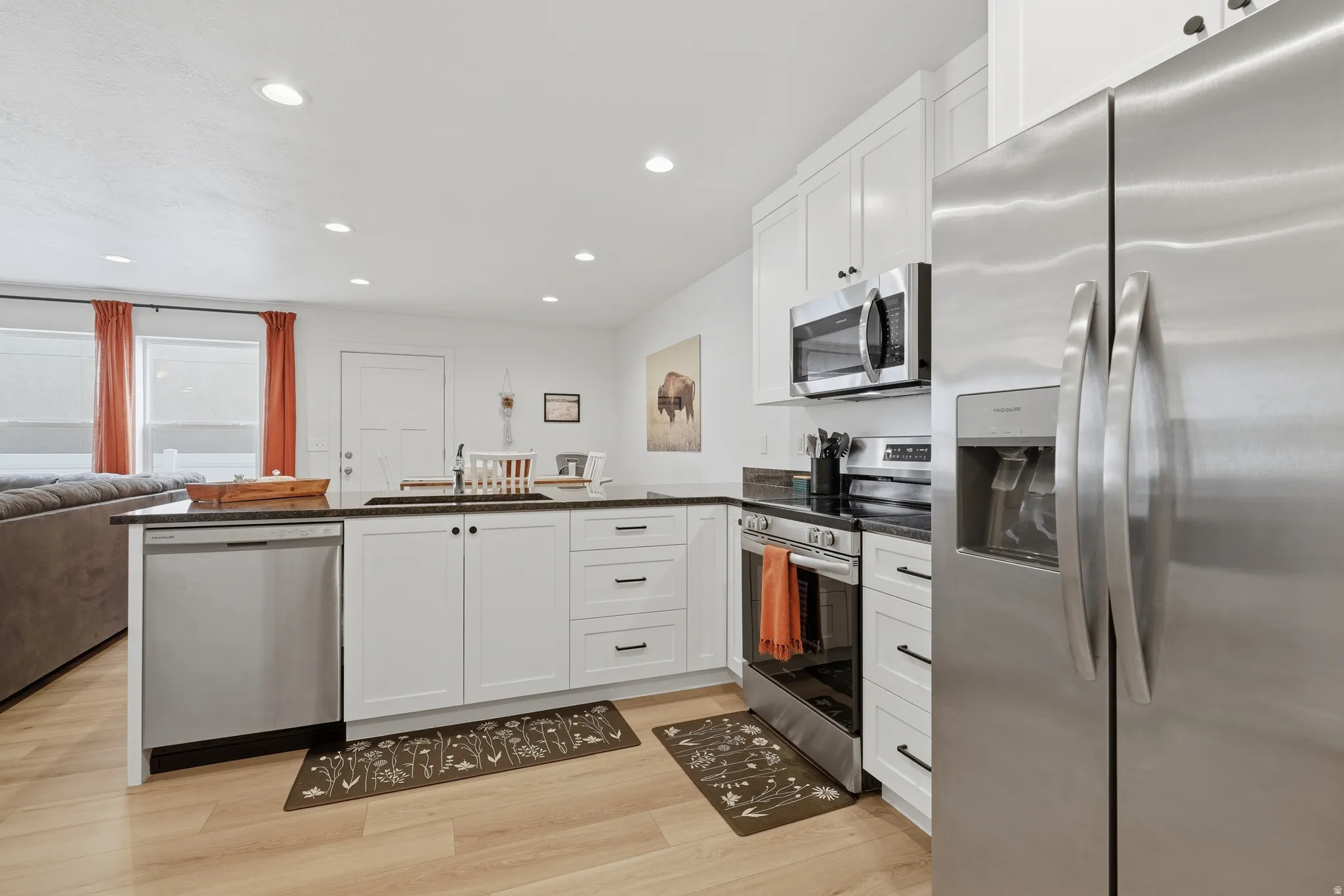 Kitchen featuring stainless steel appliances, white cabinetry, dark countertops, a central island, and wood-finish flooring