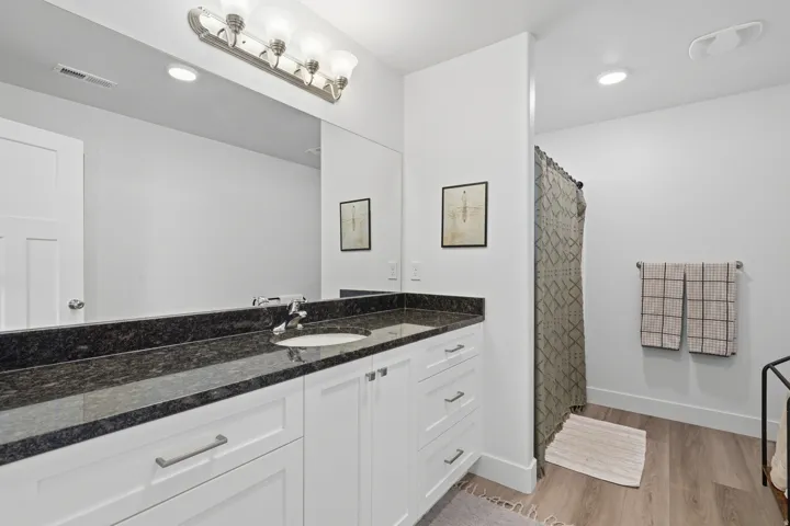 Spa-inspired primary bathroom featuring a double-sink vanity with white cabinetry, black stone countertops, and polished nickel hardware
