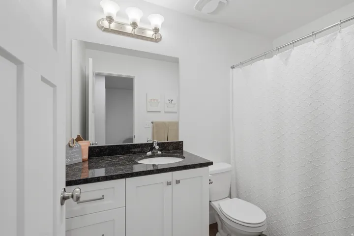 White shaker-style vanity with dark countertop, undermount sink, and brushed nickel hardware