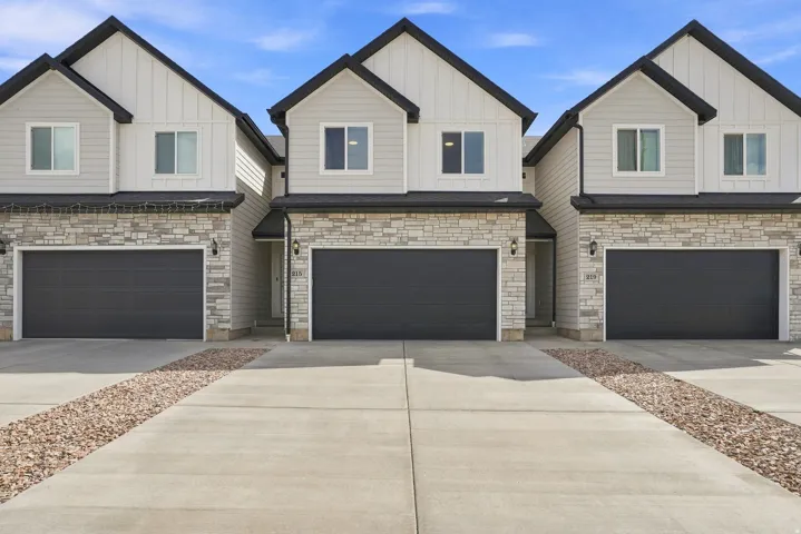 Modern exterior with board and batten siding, stone veneer accents, dark trim, and dark garage doors