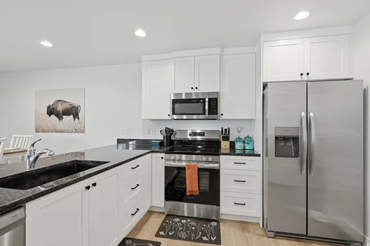 White cabinetry with black hardware, stainless steel appliances, dark countertops, a built-in sink, and wood-finish flooring