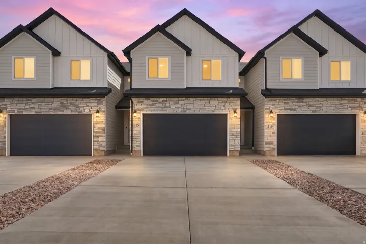 Modern exterior with stone accents and board and batten siding, featuring dark garage doors and concrete driveways with decorative rock strips