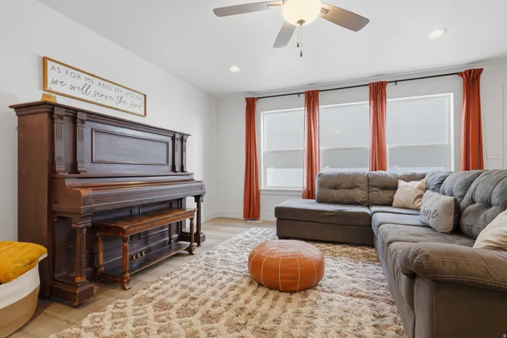 Recessed lighting, ceiling fan with integrated light fixture, three windows with roller shades, and wood-finish flooring