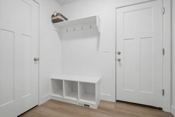 Built-in entryway bench with integrated cubbies, white wall-mounted shelf with hooks, and wood-finish flooring
