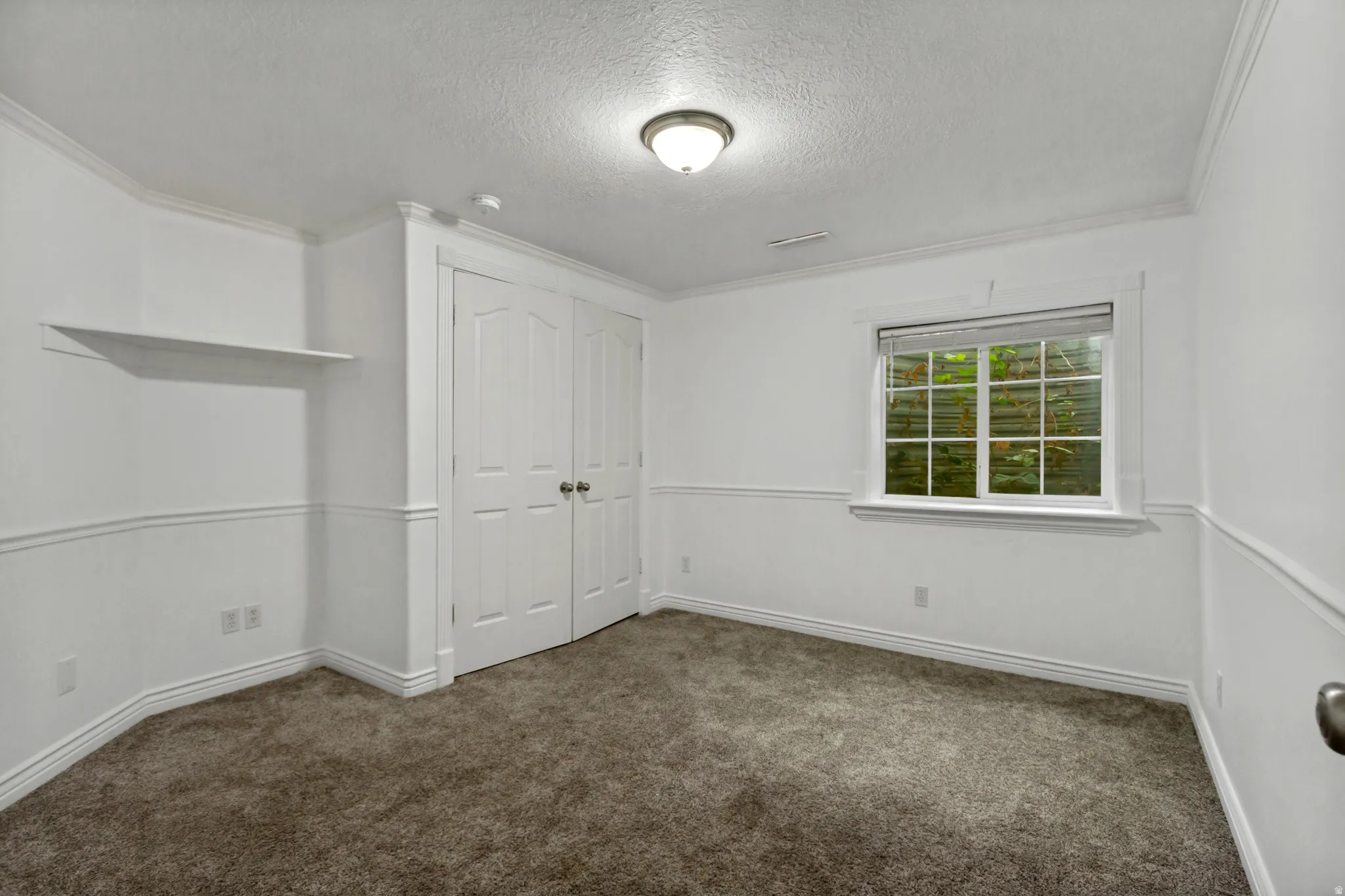 Built-in double closet with panel doors, recessed window with blinds, wall-mounted shelving, overhead lighting, and neutral carpeting