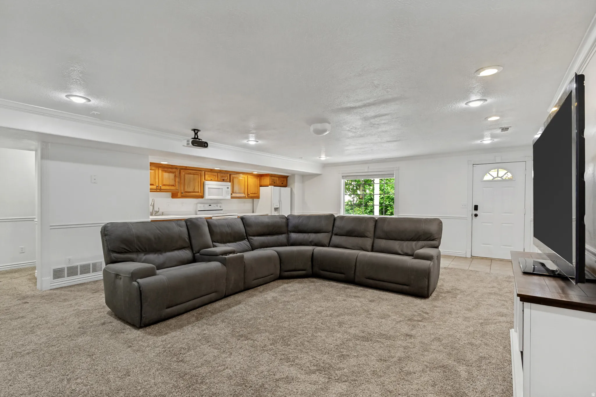 Recessed lighting illuminates the open living space, featuring a kitchen area with wood cabinetry, a white refrigerator, and a white oven