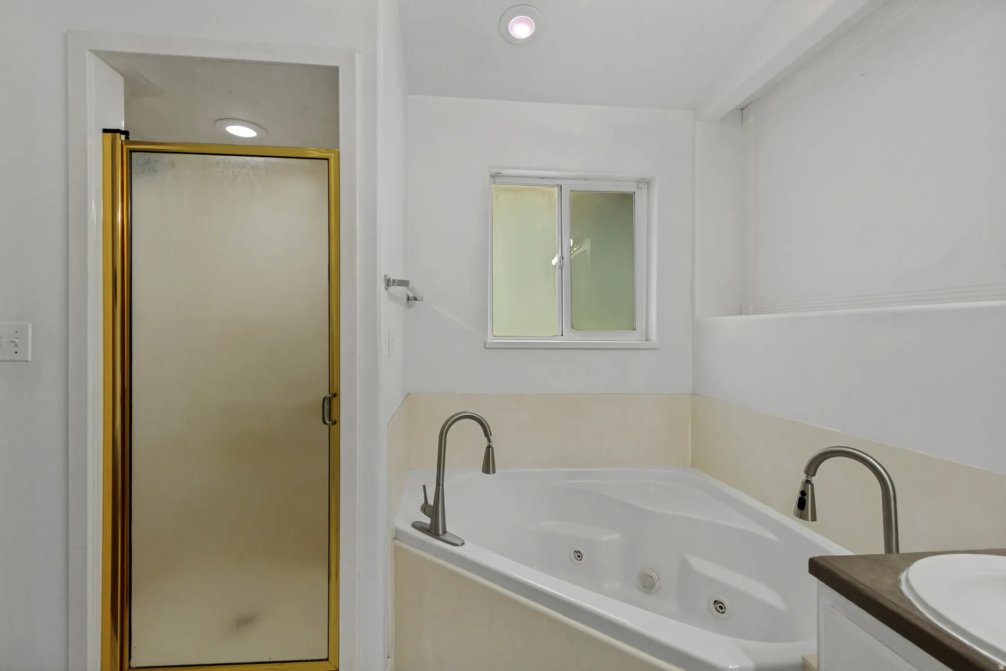 Jetted soaking tub with a gooseneck faucet, separate shower with a gold-finish frame, and recessed lighting