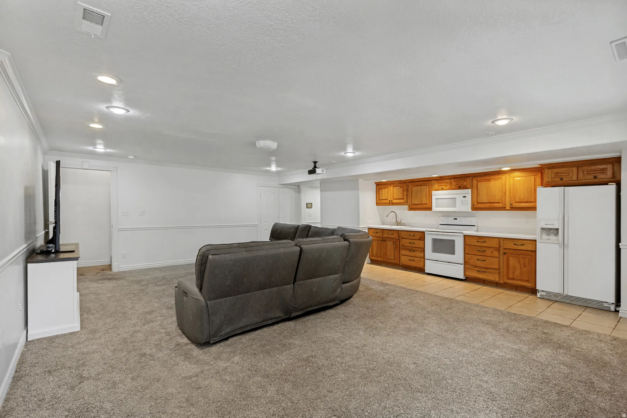 Carpeted living area with recessed lighting, integrated kitchen featuring wood cabinetry, white appliances, and a tiled floor