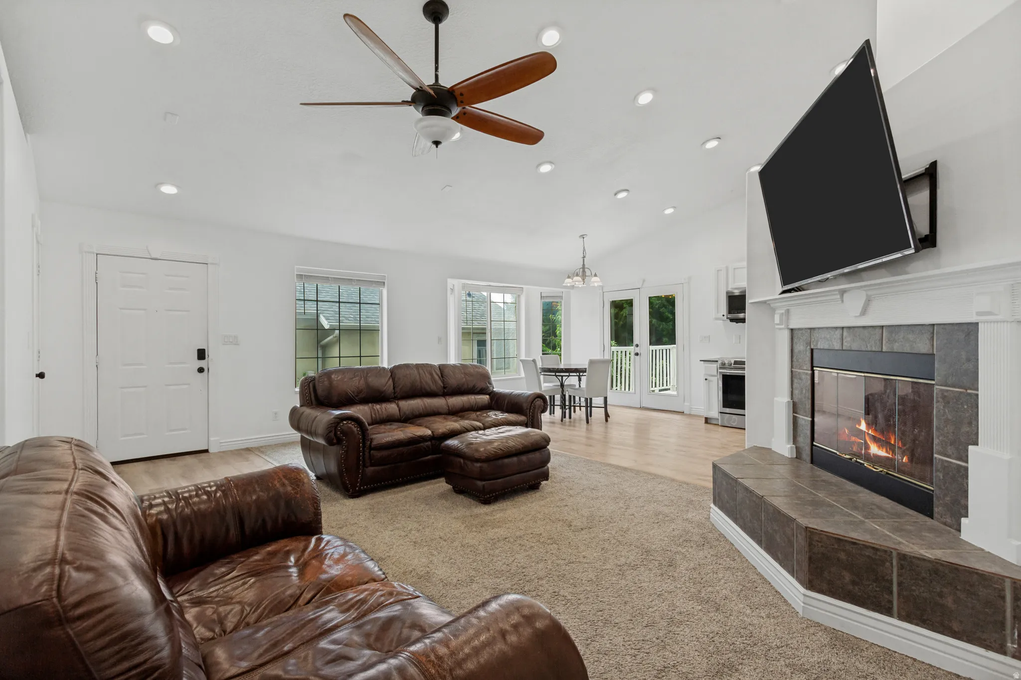 Spacious great room anchored by a wood-burning fireplace with stone surround and built-in cabinetry, ceiling fan with wood blades, recessed lighting throughout, and glass doors opening to natural light