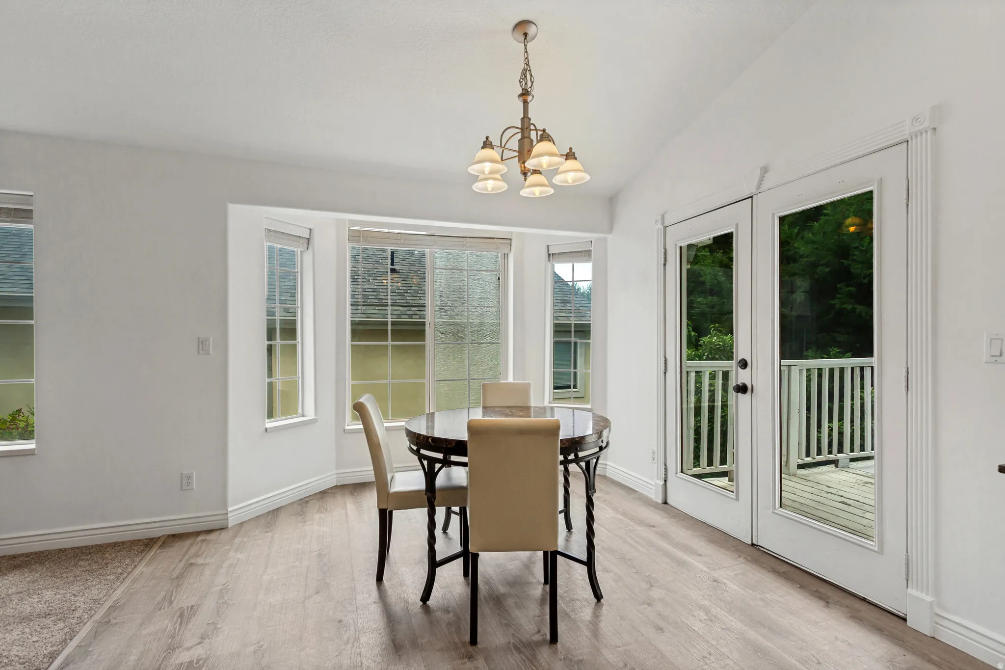 Vaulted ceiling with a decorative chandelier, bay window, wood-finish flooring, and French doors opening to a deck