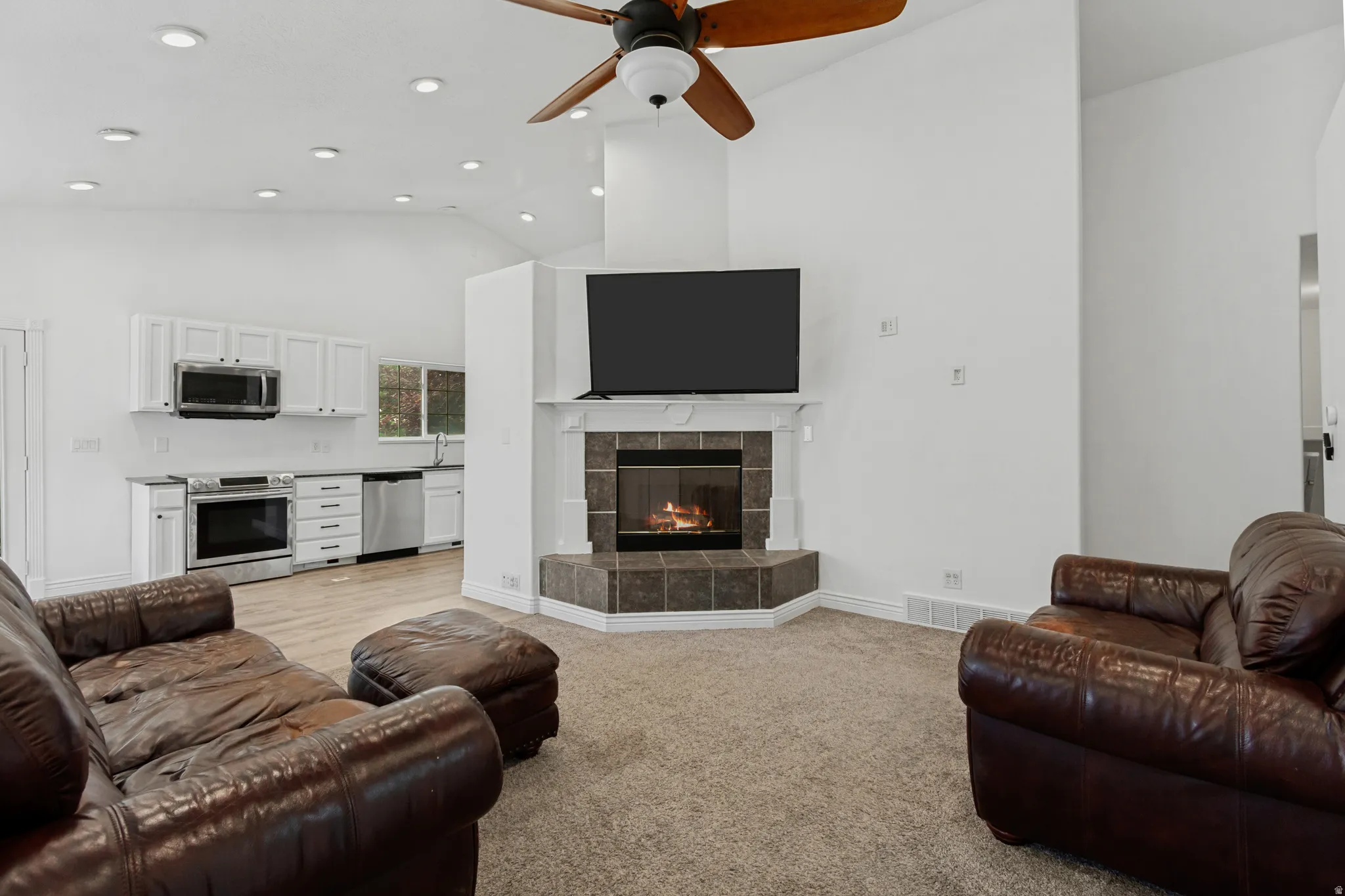 Vaulted ceilings with recessed lighting, corner fireplace with tile surround, stainless steel appliances, white cabinetry, and wood-finish flooring
