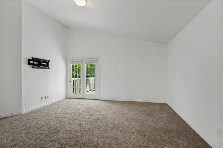 Vaulted ceiling accentuates the spacious room, featuring white walls, textured carpeting, and a built-in television mount