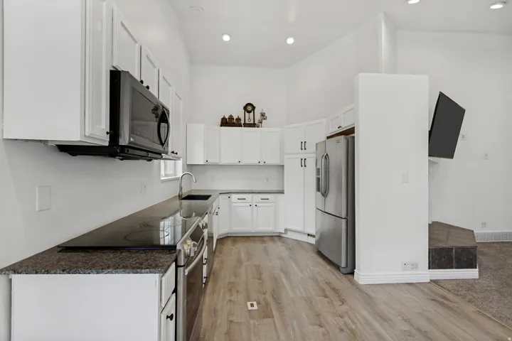 Modern galley kitchen featuring white cabinetry, stainless steel appliances including a gas range and refrigerator, dark wood-finish countertops, recessed ceiling lighting, and wood-finish flooring throughout