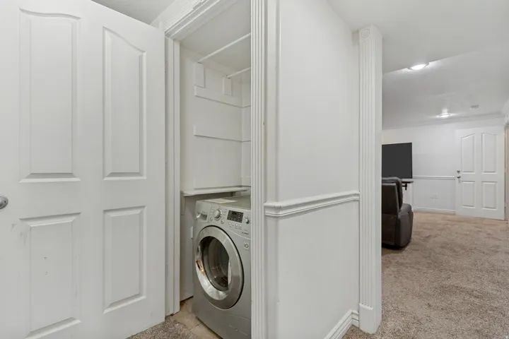 In-unit laundry appliance within a dedicated alcove, featuring built-in shelving, panel doors, and wall trim