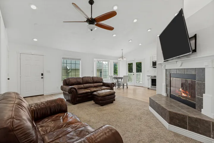 Spacious great room anchored by a wood-burning fireplace with stone surround and built-in cabinetry, ceiling fan with wood blades, recessed lighting throughout, and glass doors opening to natural light