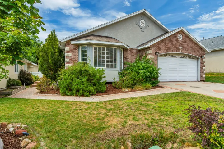 Charming brick ranch home featuring a wide front elevation with large picture windows, white garage door, and a professionally landscaped front yard with mature shrubs, flowering plantings, and a manicured lawn accented by decorative hardscape edging