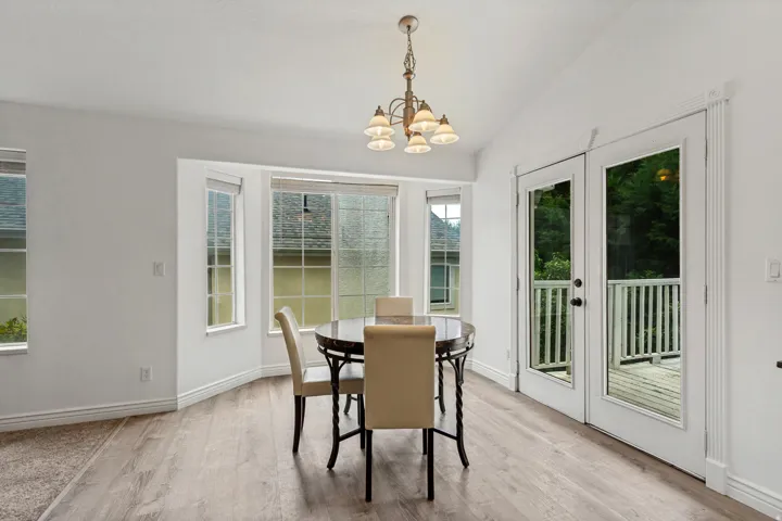 Vaulted ceiling with a decorative chandelier, bay window, wood-finish flooring, and French doors opening to a deck