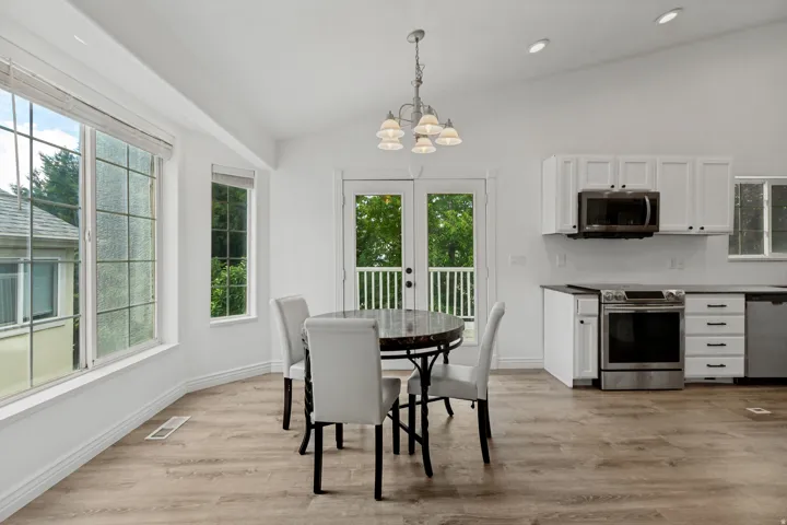 Vaulted ceiling with recessed lighting, white cabinetry, stainless steel appliances, wood-finish flooring, and double doors to an outdoor area