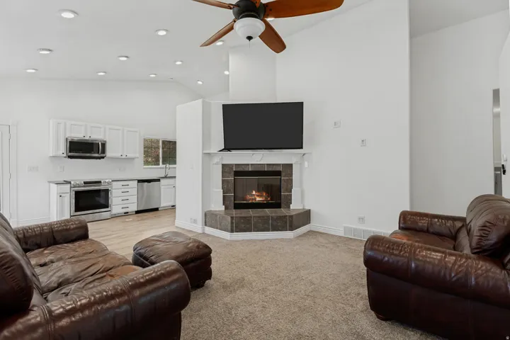 Vaulted ceilings with recessed lighting, corner fireplace with tile surround, stainless steel appliances, white cabinetry, and wood-finish flooring