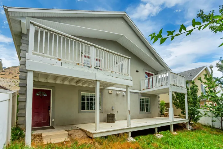 Charming two-story home featuring a covered front porch with white railings, a spacious ground-level deck ideal for outdoor entertaining, and lush landscaping with mature greenery